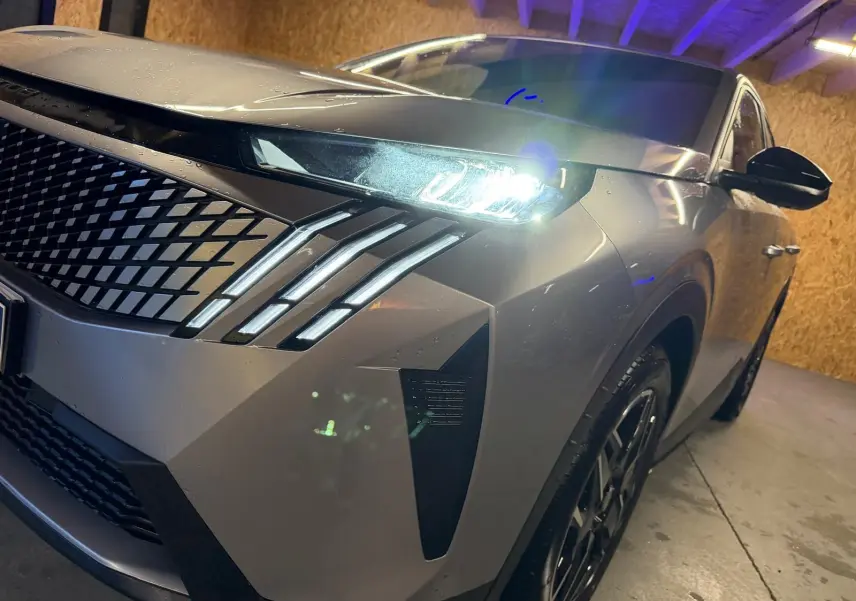 Vue 3/4 avant droit du Peugeot 3008 gris 2025 avec phares LED allumés et calandre distinctive en losanges.