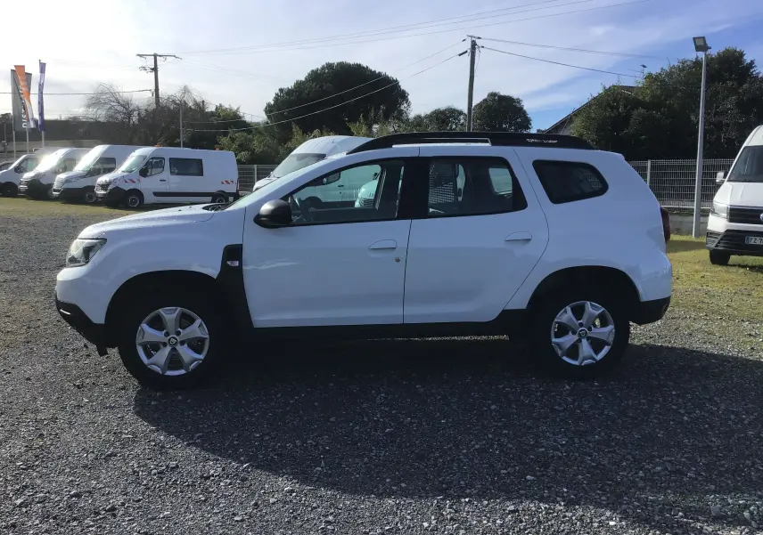 Profil côté gauche d’un Dacia Duster blanc 2021 avec jantes alliage et grille de séparation visible à l’arrière.