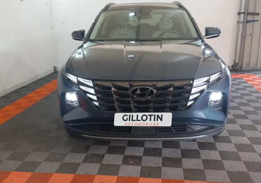 Vue avant d'un Hyundai Tucson gris foncé 2023 avec calandre noire et phares LED allumés en intérieur.