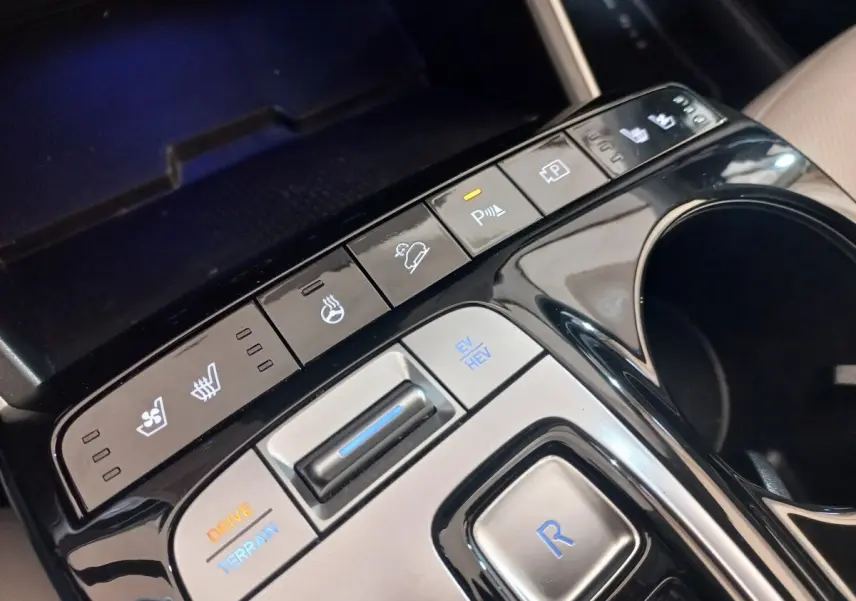 Gros plan sur la console centrale noire du Hyundai Tucson gris foncé, avec boutons de contrôle de conduite et sièges chauffants.