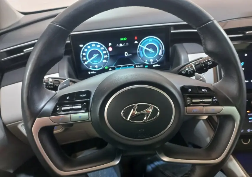 Vue rapprochée du volant cuir et alu du Hyundai Tucson 2023 avec tableau de bord numérique lumineux.