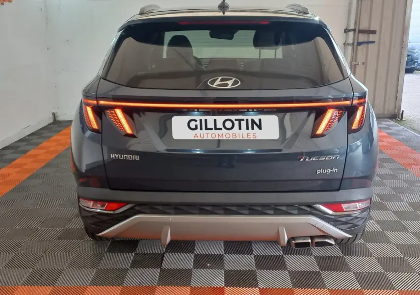 Vue arrière d'un Hyundai Tucson gris foncé 2023 avec feux LED allumés et double sortie d'échappement visible.