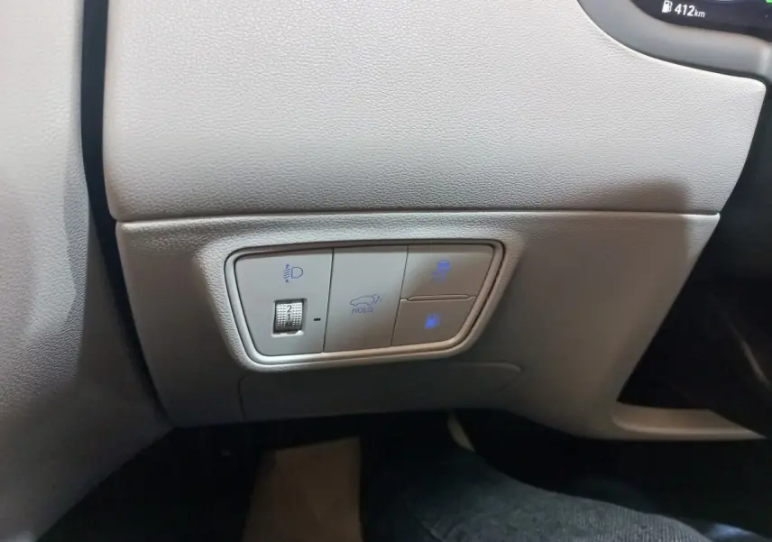 Détail des commandes de réglage des phares et fonctions de maintien sur tableau de bord gris clair du Hyundai Tucson 2023.