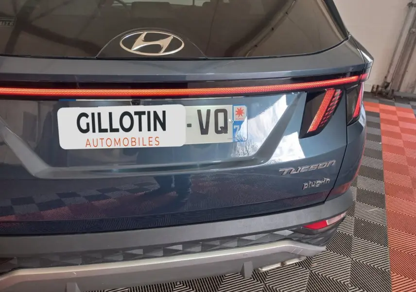 Vue arrière d’un Hyundai Tucson gris foncé 2023 avec feux LED et logo plug-in visible sur un sol à damier.