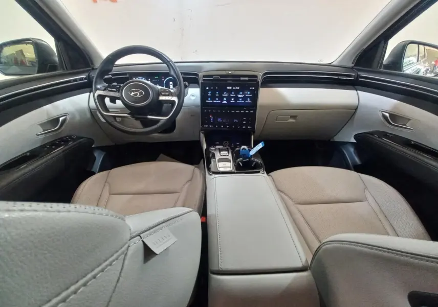 Vue intérieure avant du Hyundai Tucson 2023, tableau de bord moderne avec écran tactile et sièges beige clair.