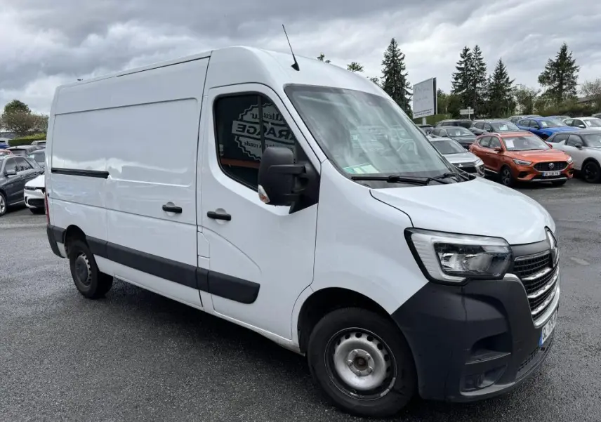 Renault Master blanc vu de 3/4 avant droit avec pare-chocs noir et roues tôlées sur parking sous ciel nuageux.