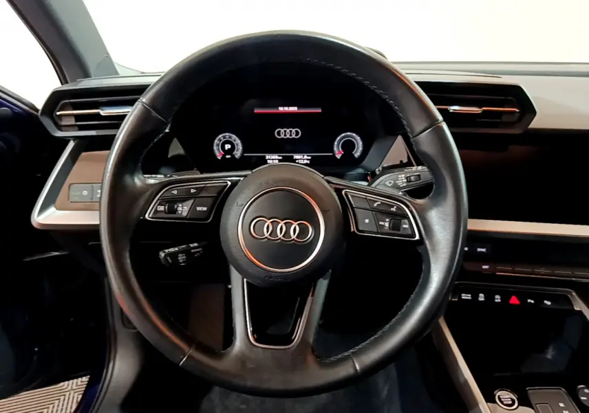 Vue centrée sur le volant cuir noir de l'Audi A3 35 TFSI 2023 avec tableau de bord numérique et détails intérieurs bleus.