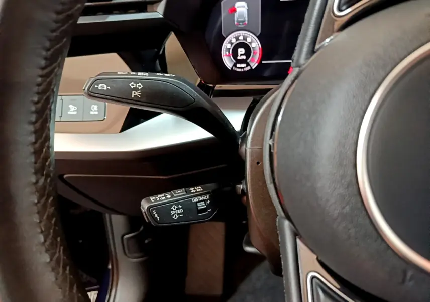 Gros plan sur la commande de régulateur de vitesse et levier de clignotant côté gauche du volant cuir d’une Audi A3 bleu 2023.