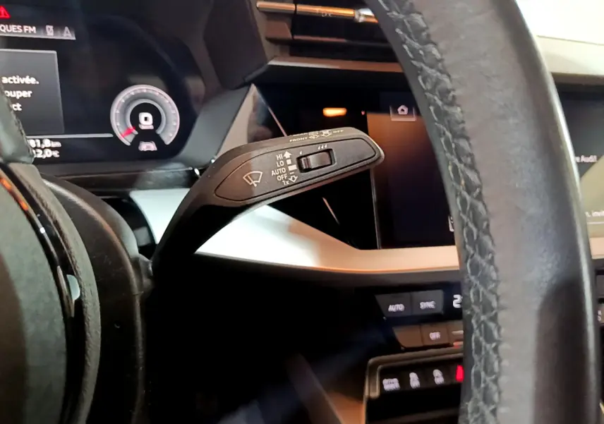 Gros plan sur la manette d’essuie-glace à gauche du volant cuir de l’Audi A3 bleu, avec tableau de bord numérique visible.
