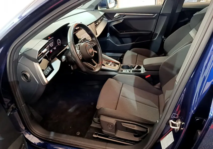Intérieur côté conducteur d'une Audi A3 bleu 2023, volant cuir et tableau de bord numérique avec écran tactile.