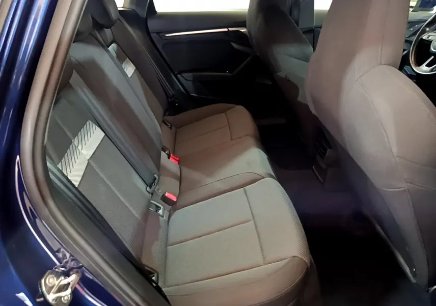 Vue intérieure côté gauche sur la banquette arrière grise d'une Audi A3 35 TFSI bleu 2023 avec portes ouvertes.