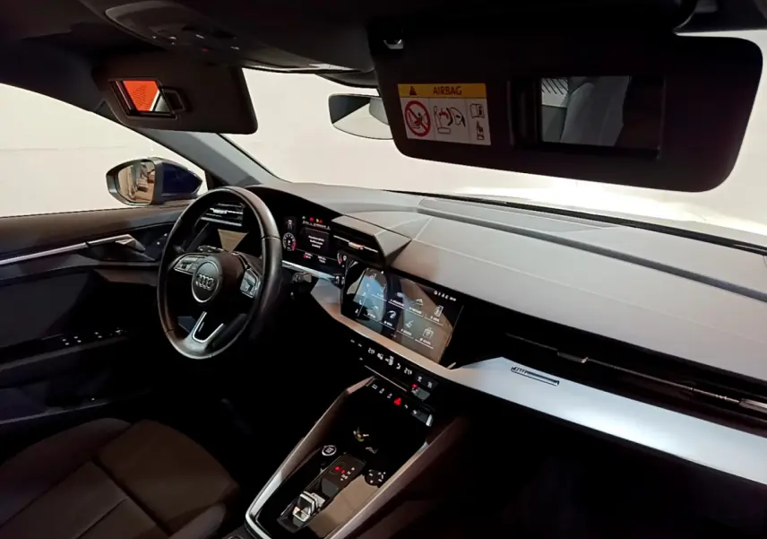 Intérieur de l'Audi A3 2023 vu côté conducteur, tableau de bord moderne avec écran tactile et volant cuir noir.