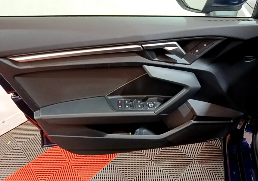 Vue rapprochée de la porte côté conducteur bleu foncé de l'Audi A3 35 TFSI 2023 avec commandes de vitres et rétroviseurs.