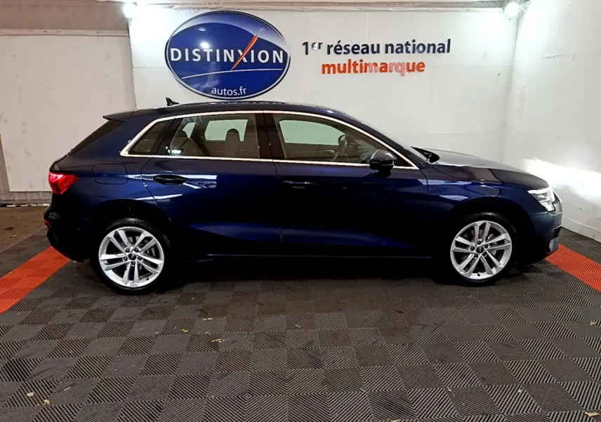 Profil latéral droit d'une Audi A3 35 TFSI bleu foncé, stationnée en intérieur sur sol carrelé gris et rouge.