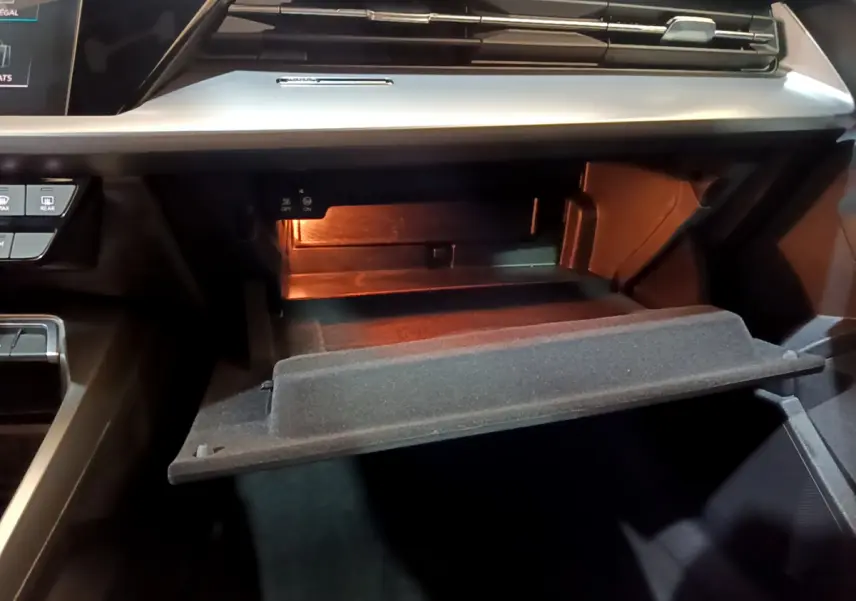 Ouverture de la boîte à gants éclairée côté passager dans l'habitacle noir de l'Audi A3 bleu 2023.