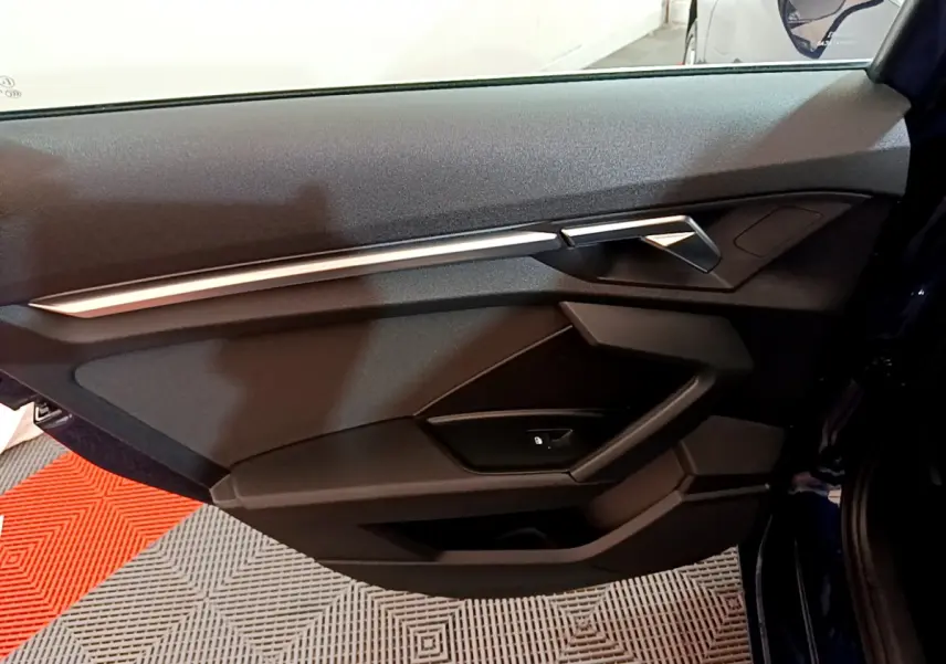 Vue intérieure côté gauche de la porte avant d'une Audi A3 35 TFSI bleu avec garniture noire et insert argenté.