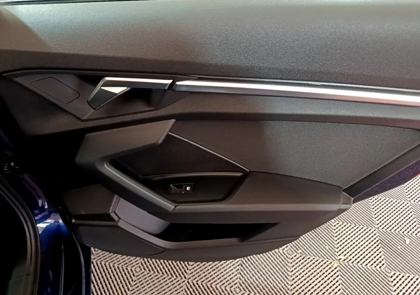Gros plan sur la porte côté gauche bleu foncé d'une Audi A3 35 TFSI 150 MHEV avec poignée et commandes intégrées.