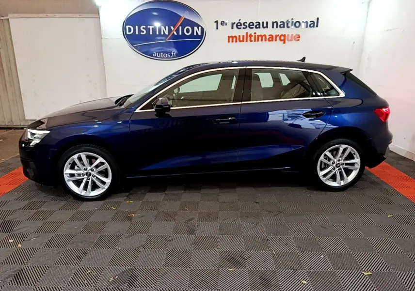 Profil côté gauche d'une Audi A3 35 TFSI hybride bleu foncé, stationnée en intérieur sur sol damier noir et rouge.