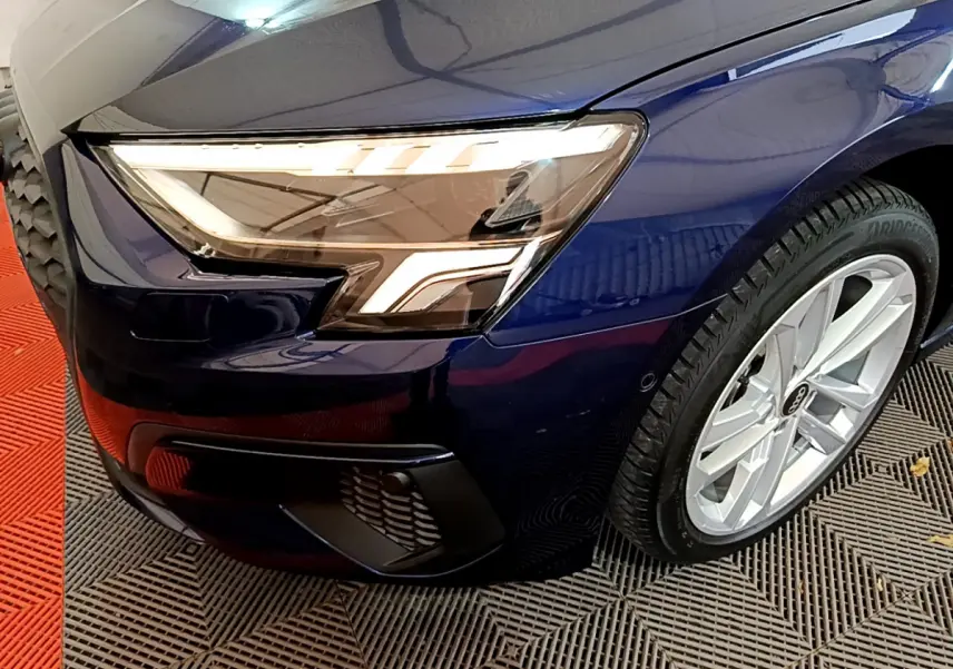 Gros plan sur l'avant droit bleu d'une Audi A3 35 TFSI 150 MHEV avec phares LED et jante argentée.