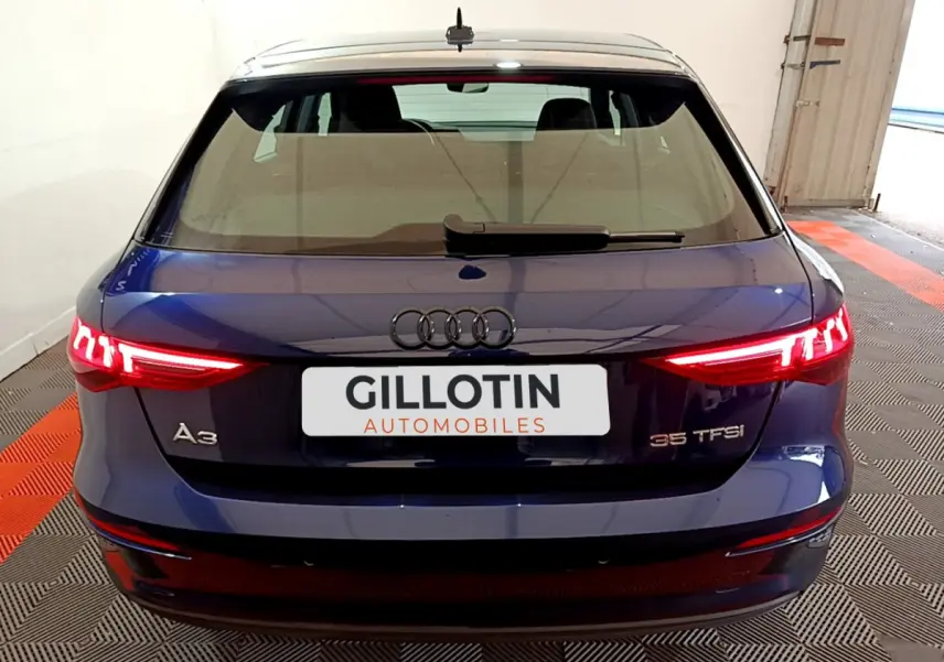 Vue arrière d'une Audi A3 35 TFSI bleu nuit avec feux arrière LED allumés dans un garage.