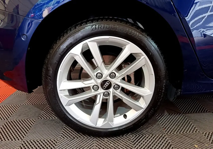 Gros plan sur la roue avant gauche d'une Audi A3 bleu 2023 avec jante alliage argentée à design moderne.