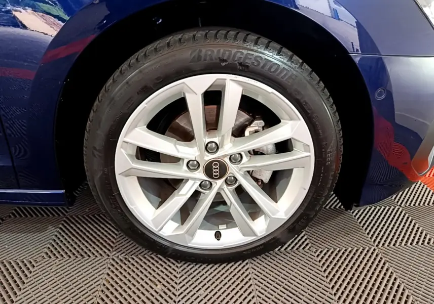 Gros plan sur la roue avant gauche d’une Audi A3 bleu 2023, avec jante argentée et logo Audi au centre.