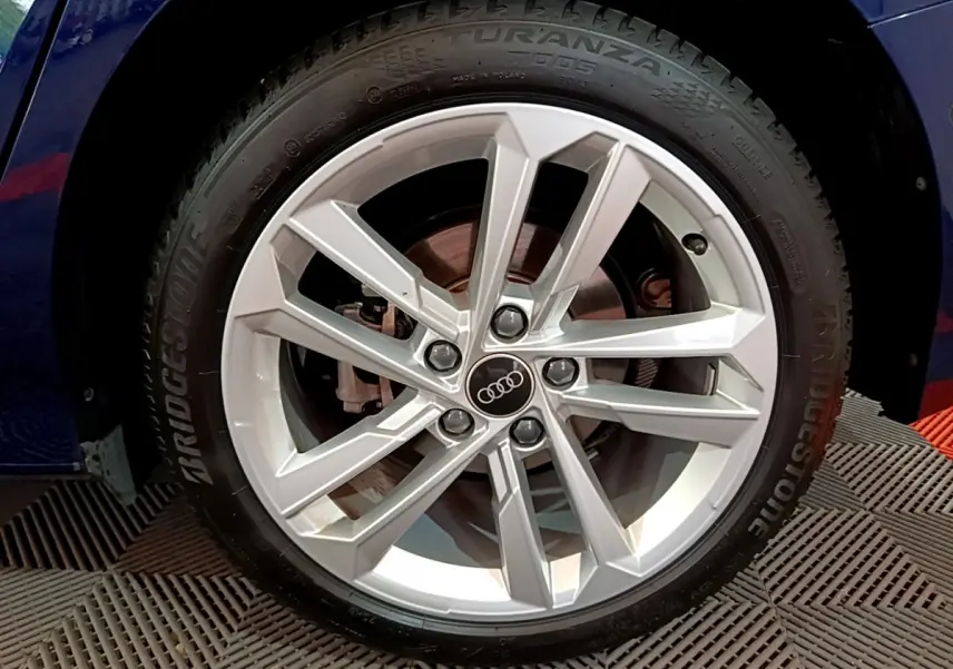 Gros plan sur la roue avant gauche de l'Audi A3 bleu 2023 avec jante alliage et logo Audi au centre.