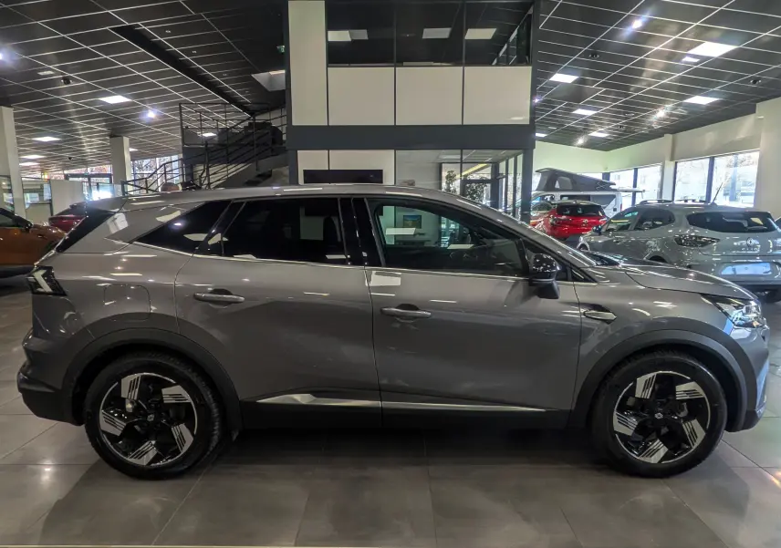 Vue latérale droite du Renault SYMBIOZ E-TECH Full Hybrid gris Cassiopé en showroom, soulignant ses jantes biton noires et argentées.