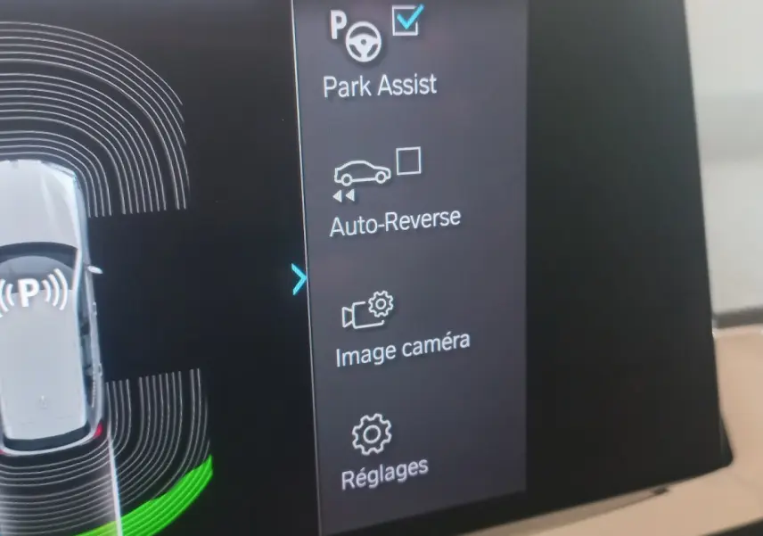 Écran tactile intérieur du BMW X3 blanc montrant les options d’aide au stationnement et caméra.