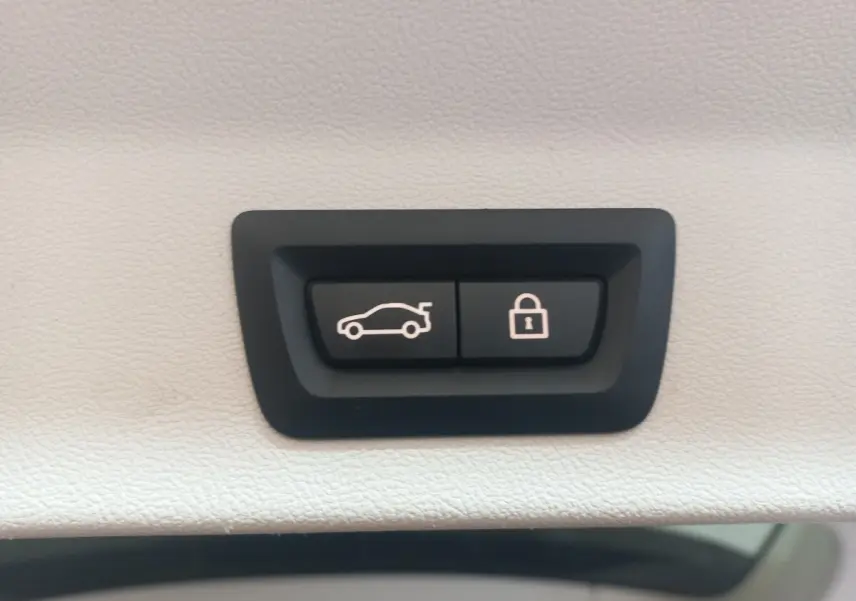 Gros plan sur les boutons d'ouverture et de verrouillage du coffre, intérieur blanc du BMW X3 hybride rechargeable.