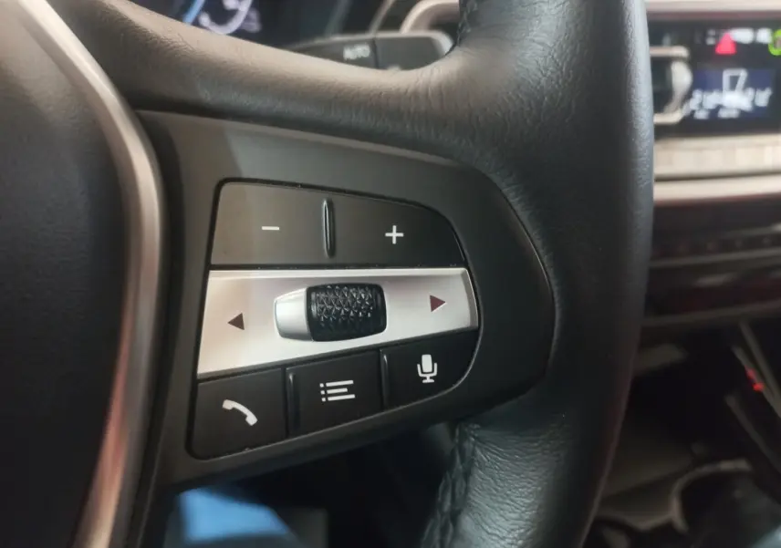 Gros plan sur les commandes multifonctions en cuir noir du volant du BMW X3 xDrive30e blanc, intérieur moderne.