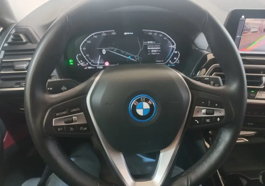 Vue intérieure centrée sur le volant cuir noir du BMW X3 xDrive30e avec tableau de bord digital et écran tactile.
