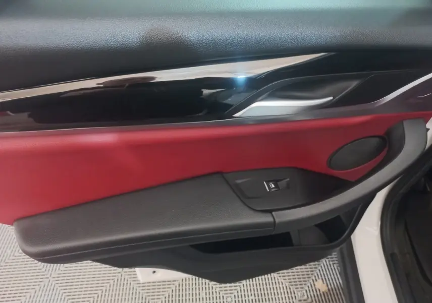 Vue intérieure côté gauche de la porte avant d’un BMW X3 blanc, avec garniture rouge et noire et poignée argentée.