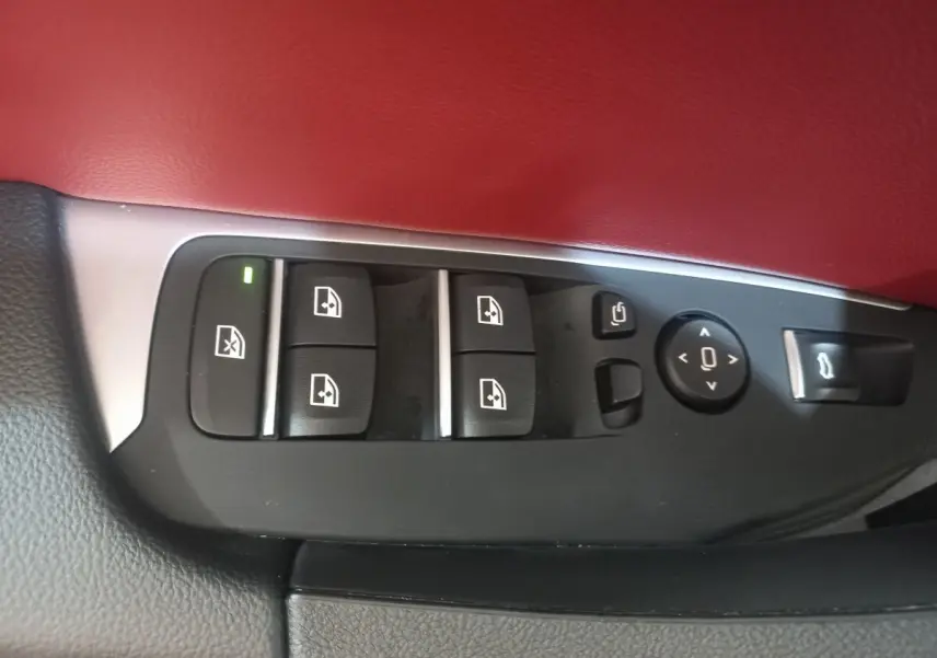 Gros plan sur les commandes des vitres et rétroviseurs côté conducteur, garniture cuir rouge et noir visible.
