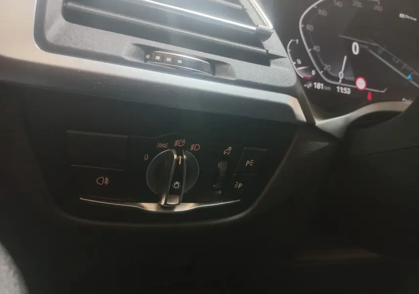 Gros plan sur le commodo des phares et tableau de bord numérique côté gauche d'une BMW X3 blanche hybride rechargeable.