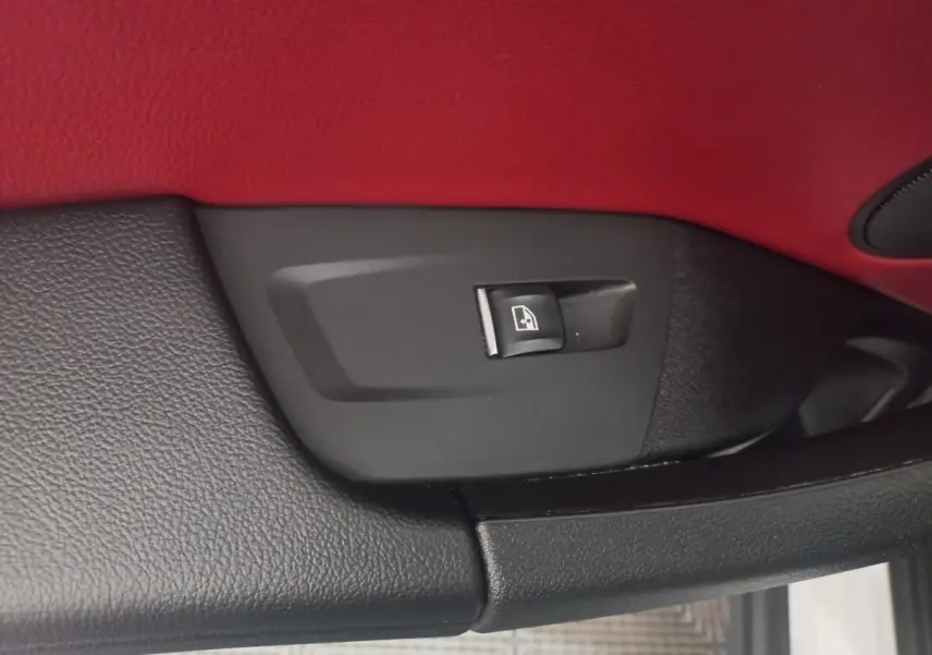 Gros plan sur le bouton de commande de lève-vitre dans l’habitacle rouge et noir d’un BMW X3 blanc.