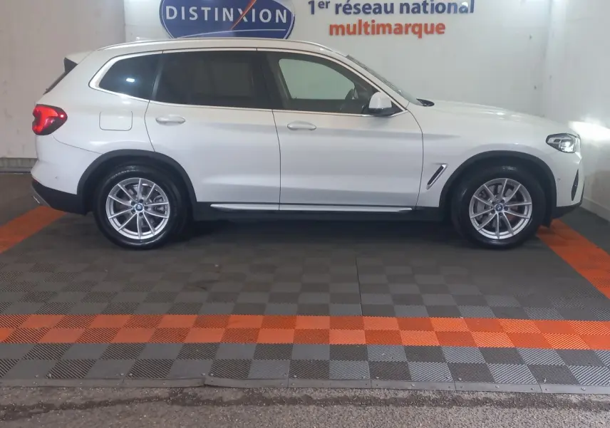 Vue de profil côté gauche d’un BMW X3 blanc hybride rechargeable garé en intérieur avec jantes alliage et feux arrière allumés.