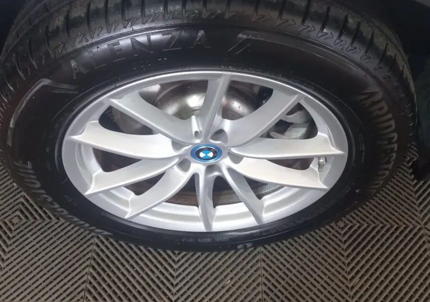 Gros plan sur la jante argentée et le pneu Bridgestone d’un BMW X3 blanc, mettant en valeur le logo central bleu.