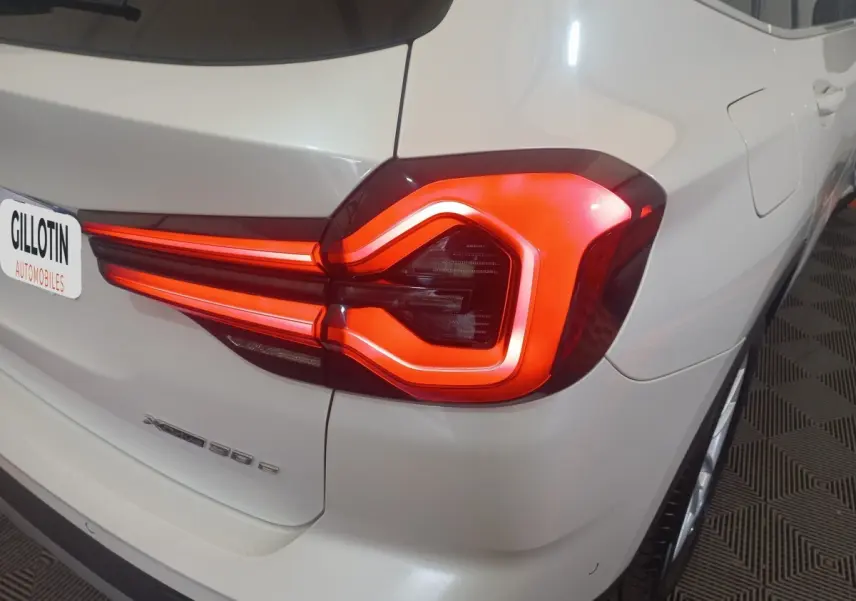 Feu arrière droit allumé d’un BMW X3 xDrive30e blanc, vue en gros plan sur l’arrière droit.