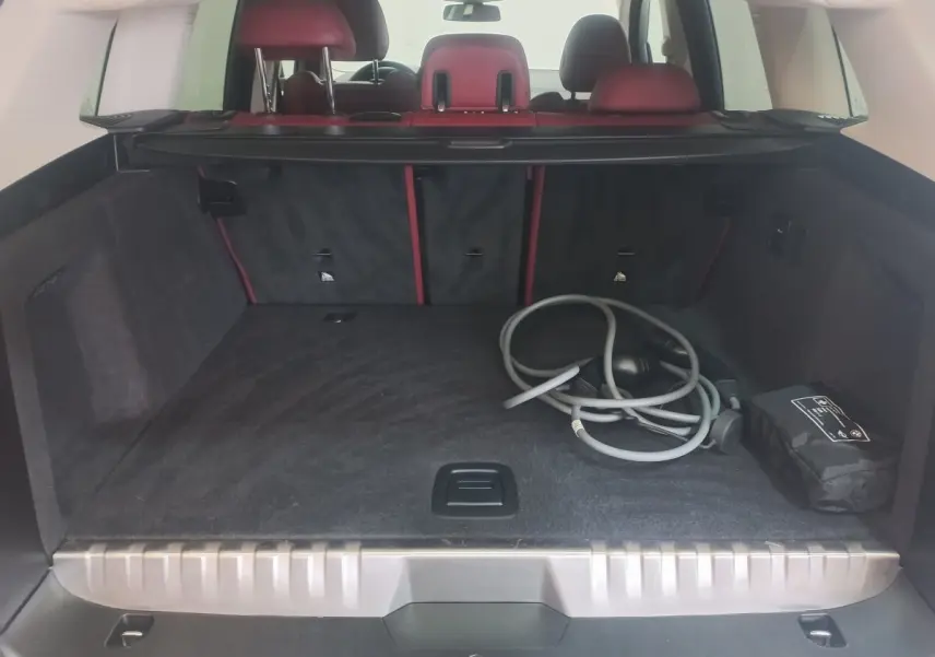 Coffre ouvert vu de l'arrière du BMW X3 blanc, avec câbles de recharge et sièges arrière rouges visibles.