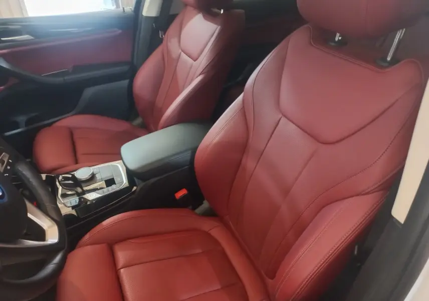 Vue intérieure côté conducteur du BMW X3 blanc 2022, sièges avant en cuir rouge et console centrale moderne.