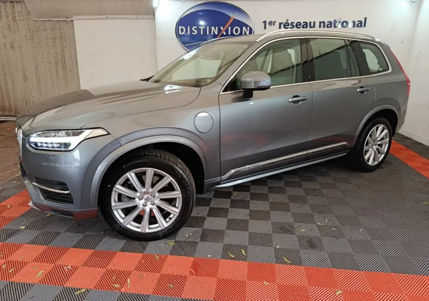 Vue de profil côté gauche d'un Volvo XC90 gris clair hybride rechargeable stationné en intérieur avec jantes alliage visibles.