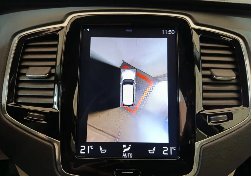 Écran tactile central montrant vue aérienne du Volvo XC90 gris clair en stationnement, tableau de bord noir brillant.