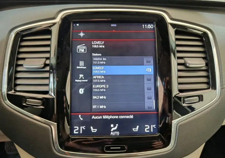 Écran tactile central du tableau de bord du Volvo XC90 gris clair, affichant les stations radio FM.