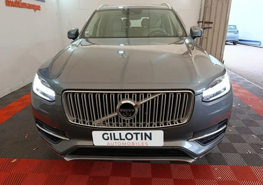 Vue frontale d'un Volvo XC90 gris clair avec calandre verticale chromée et phares LED allumés.