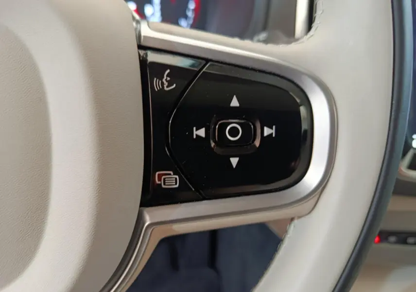 Gros plan sur les commandes noires du volant cuir beige du Volvo XC90 T8 hybride rechargeable, côté gauche.