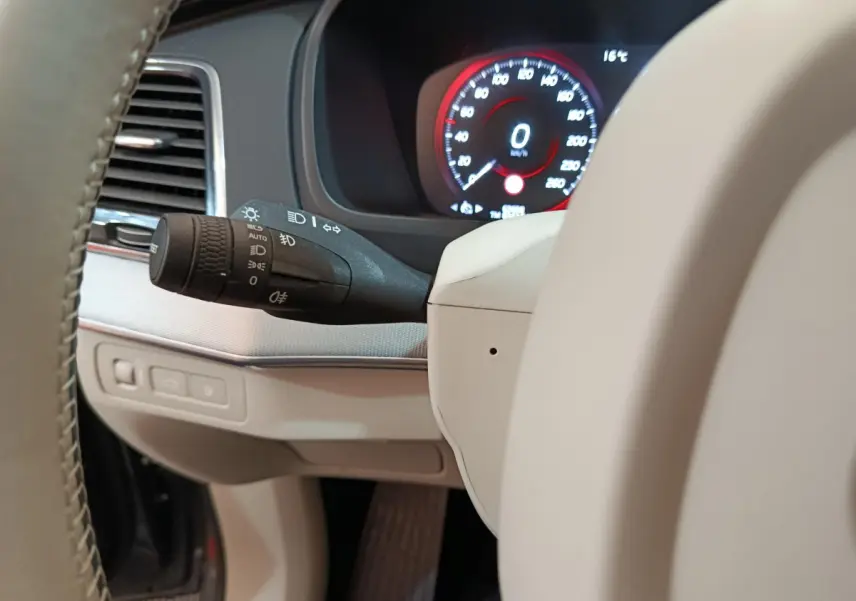 Détail du commodo d'éclairage et tableau de bord numérique affichant 0 km/h dans un Volvo XC90 T8 gris clair.