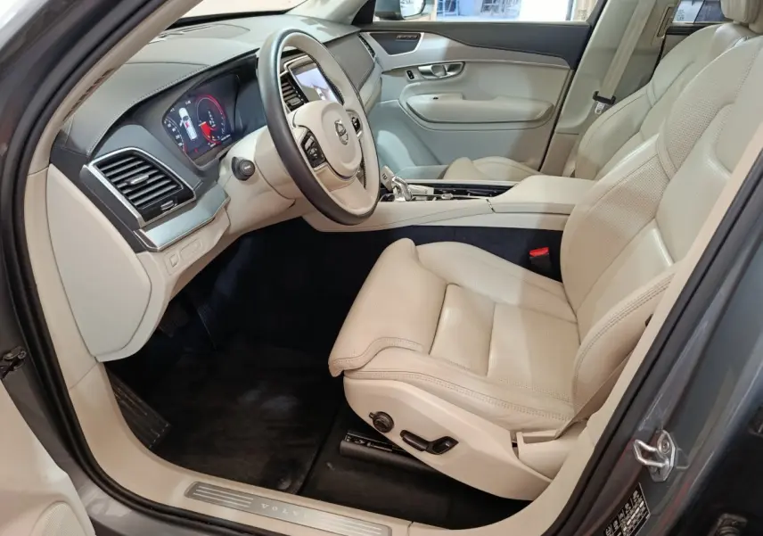 Intérieur côté conducteur du Volvo XC90 gris clair, sièges cuir beige et tableau de bord moderne avec écran digital.