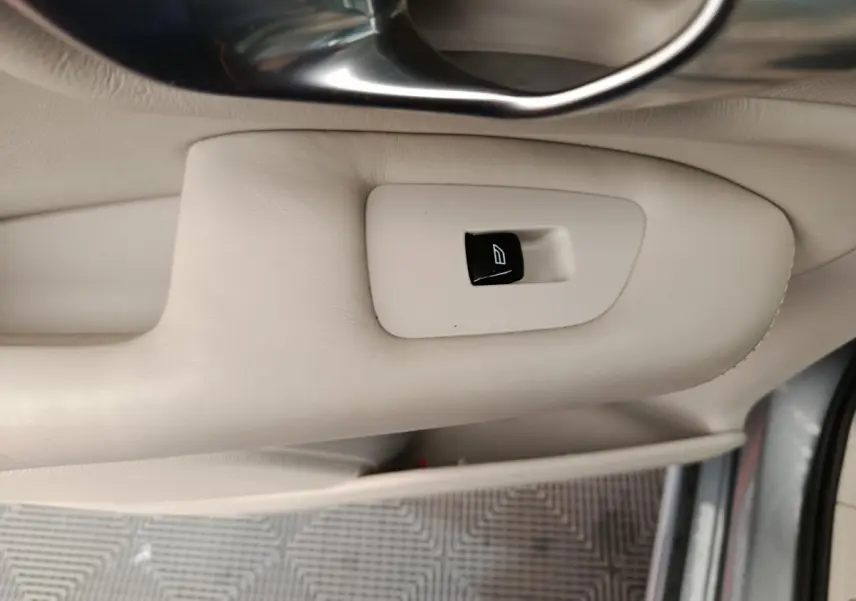Bouton de commande de lève-vitre sur la porte intérieure beige du Volvo XC90 gris clair, vue côté conducteur.
