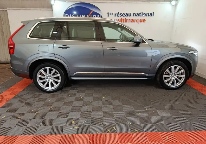 Vue de profil côté gauche d'un Volvo XC90 gris clair, SUV hybride rechargeable avec jantes alliage et toit ouvrant.